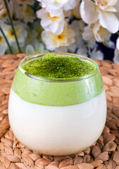 Dalgona Matcha Latte with sakura flowers on a wicker background.