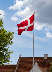 Danish flag with blue sky and clouds, standing with tress by its side