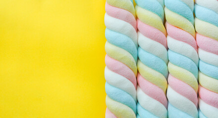 top view of twisted pastel color marshmallow on yellow background with copy space, flat lay