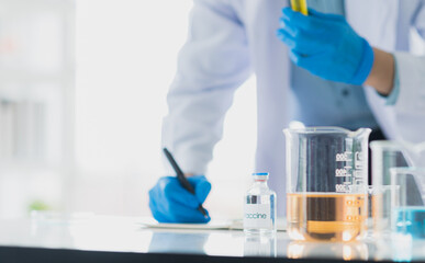Professional Asian scientist or researcher man in work coat uniform writing a result of experiment and holding colorful sample in test tube in science lab