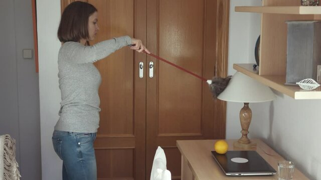 Woman cleaning in bedroom with a feather duster