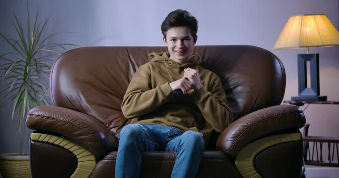 Happy boy making victory gesture as team scoring goal in TV match. Portrait of cheerful Caucasian teenage fan cheering at home as watching soccer or football match. Cinema 4k ProRes HQ.