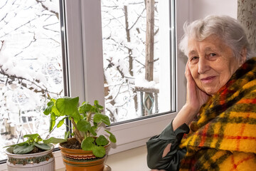 Old lonely woman sitting near the window in his house.