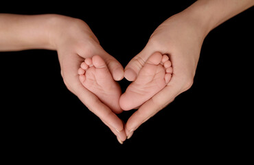 Tiny feet on female Heart Shaped hands closeup. Mamas arms in heart shape holding legs of newborn baby.