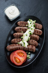 Black plate with grilled serbian cevapi or cevapcici sausages and kajmak cheese, vertical shot, selective focus