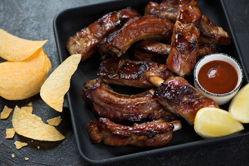 Close-up of a cast-iron serving tray with sliced bbq pork ribs and potato chips, selective focus