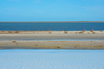 Symmetrical minimalism coastal landscape with blue water, sand, 
clear horizon and cloudless sky. 
Lines and stripes in the coastal wild landscape. Sea, lake and sand spit. 