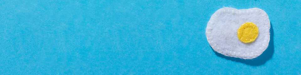 Toys in the form of fried egg  hand made of felt on blue background. Hand sewing. copy space