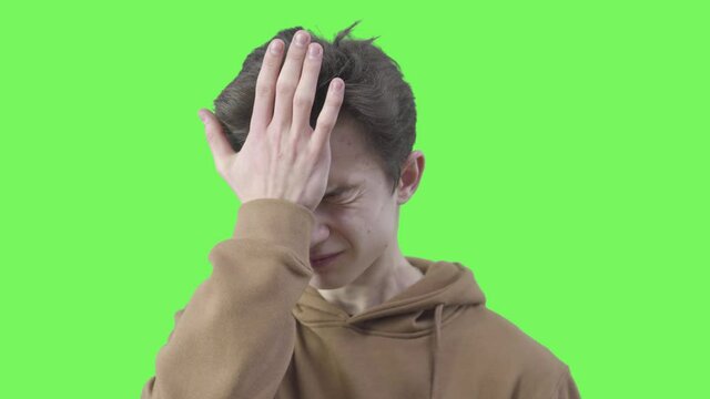 Close-up of boy making facepalm gesture. Portrait of shocked Caucasian teen expressing epic fail emotion. Chromakey, green screen background.