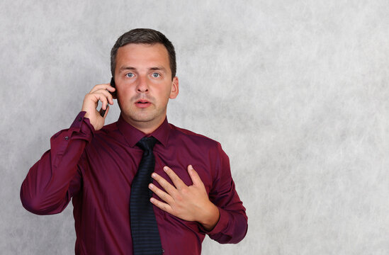 An alarmed man in a red shirt is talking on the phone.