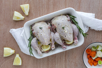raw coquelet chickens prepared for roasting with vegetables and herbs