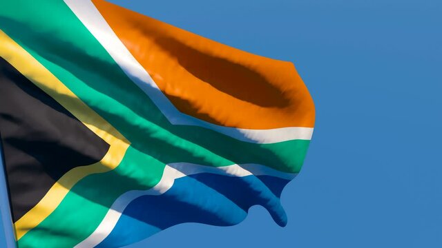 The national flag of South Africa flutters in the wind against a blue sky