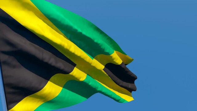 The national flag of Jamaica flutters in the wind against a blue sky