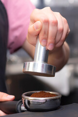 close-up photo of female hands holding a metal tamper and a portafilter with coffee in a coffee shop. barista preparing for pressing ground coffee for brewing espresso. vertical photo