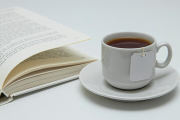 Reading a book over a mug of hot tea. An open book, a white mug with black tea. Free space for insertion.