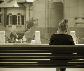 Young blonde girl sitting on a bench. Vintage look of a lonely girl on a bench