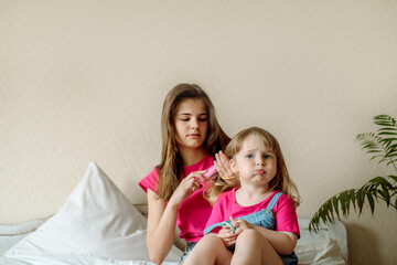 Happy young girl combing hair in the morning at home.Two teenage girls and baby sisters are caring...