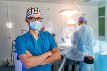 Doctor stands crosshands in medical mask. Medical team on background. Doctor in glasses with medical mask on face. Close up shot.