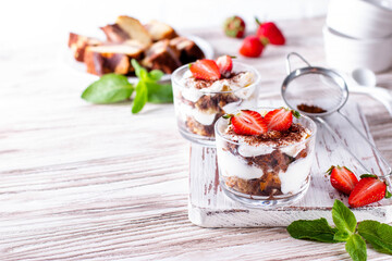 Layered dessert parfait in a glass with strawberries, sponge cake and whipped cream. Copy space