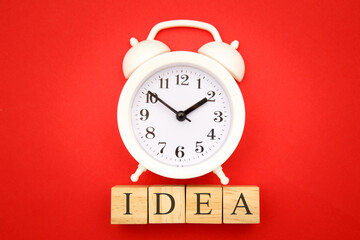 IDEA word made of wooden cubes, business concept. Four wooden cubes and alarm clock on red background.
