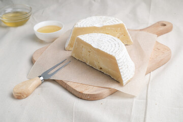 Homemade cheese on wooden plate at light background.