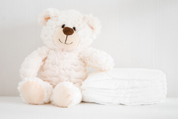 Teddy bear sitting beside stack of new white diapers. Front view. Closeup.