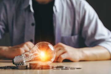 Asian Men and their hopes for idea saving energy and accounting finance. ways to adjust your budget to this New Normal concept. light bulb and money stack on wood table and on black background.