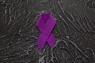 Purple ribbon on dark grey background, top view with space for text. Domestic violence awareness.