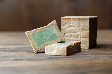 Bar and two slices of traditional aleppo organic laurel soap on a brown wooden background.