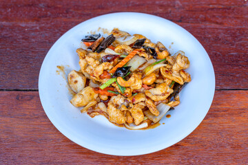 Stir Fried Chicken with Cashew Nuts Thai food on a white plate on a brown table.