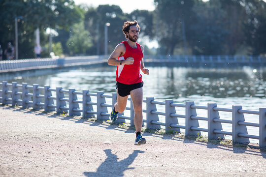 Hombre joven practicando running en el parque junto a un lago