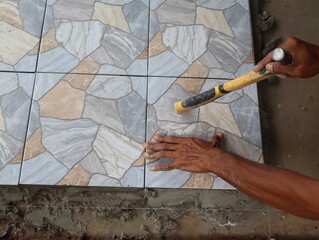 The plasterer works tapping tiles with Tile Mallet for better gluing.