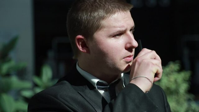 Man communicates on a walkie-talkie wearing a jacket and a white shirt. The guard speaks on a walkie-talkie.