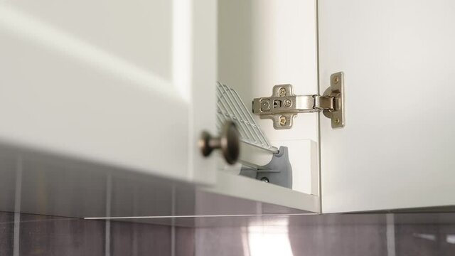 A man opens an empty kitchen cupboard for storing dishes. Empty cupboard in the kitchen.