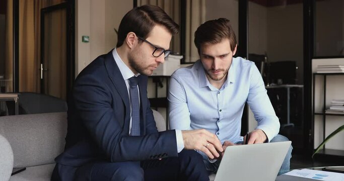 Two executive businessmen working together analyzing financial market in modern office. Serious business partners discussing online project doing digital trade strategy research using laptop computer.