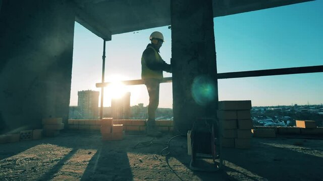Construction site, construction industry, construction worker concept. Male engineer sands walls with a machine.