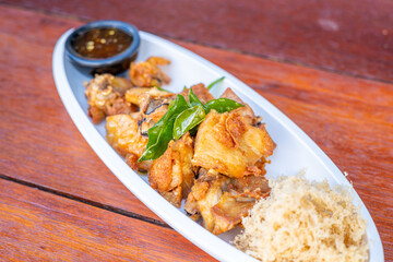 Yellow herbal fried chicken with chicken sauce on a white plate on a brown table
