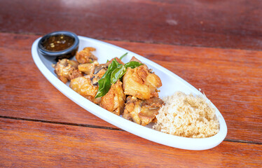 Yellow herbal fried chicken with chicken sauce on a white plate on a brown table