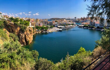 Fototapeta na wymiar Agios Nikolaos Lake View Point. Lookout Point at Beautiful Lake with rocks, greenery and colorful city buildings.