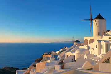 Traditional whitewashed windmills, hotels and apartments in Oia village, Santorini island, Greece on a sunset.