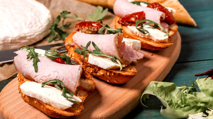 Appetizers table with italian antipasti snacks. Bruschetta with brie cheese, arugula and sun-dried tomatoes, ham. Food recipe background. Close up