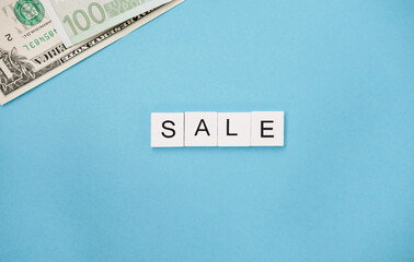 The Word Sale are spelled out in wooden letter tiles and banknotes on a blue trendy background. promotion seasonal offer ads.