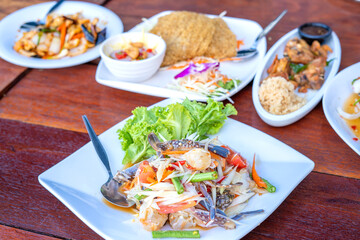 Papaya salad with fresh blue swimming crab, put papaya in a white dish and Thai food on a brown table in a restaurant