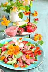 salad with nasturtium flowers and leaves with strawberries and avocados. dressed with strawberry vinaigrette or strawberry dressing with poppy seeds.