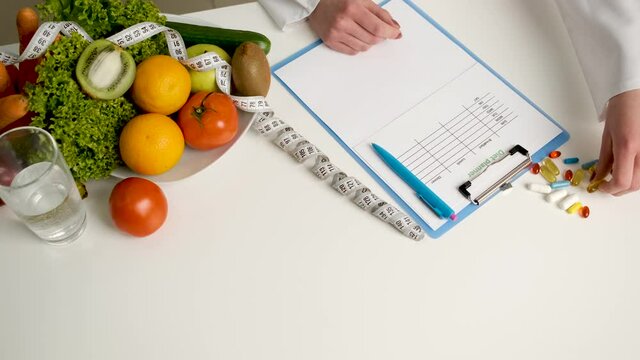 A nutritionist writes a prescription for health pills on his desk. Vegetables and fruits on the table