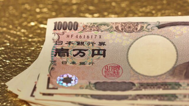 Close-up slide video of 100,000 yen in cash sent by the Japanese govt of Abe Shinzo to fight economic unemployment crisis caused by COVID-19 on a golden background.