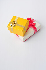 Two gift boxes with bows white with a red ribbon in white peas and yellow with a gold ribbon, stacked on top of each other on a white background.