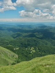 Obraz premium beautiful landscape seen from top of the green mountain in summer season. horizon line on sunny day with blue sky and fluffy clouds