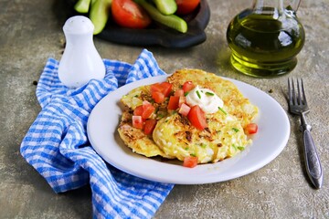 Cabbage fritters with green onions, tomatoes and mayonnaise on a white plate on a gray concrete background. Cabbage recipes. Vegetarian recipes, vegetable dishes.