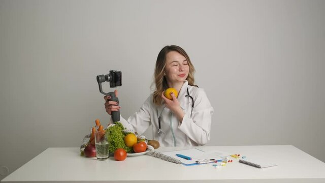 A doctor-nutritionist at his desk conducts online training for his clients by video call over the phone holding an orange. Healthy Eating